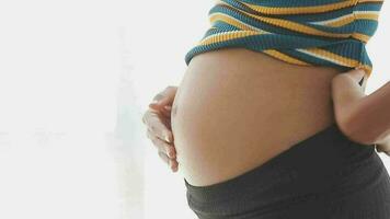 Young beautiful pregnant woman standing near window at home video