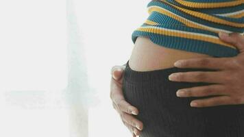 Young beautiful pregnant woman standing near window at home video