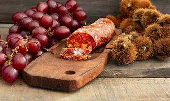 cerca arriba castañas chorizo y uvas en rústico de madera mesa foto