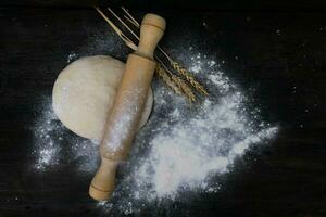 rolling pin with wheat flour dough on wood photo