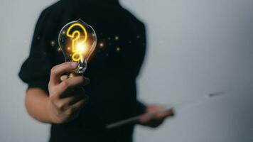 Hand holding light bulb with question mark icon on a dark background problem solving searching for answers. photo