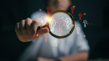 The concept of finding an answer to complex questions in business. Hand holding a magnifying glass with a question mark. photo