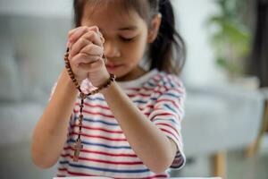 Christian concept. Little Asian girl praying withholding the cross. Concepts of hope, faith, Christianity, religion, photo