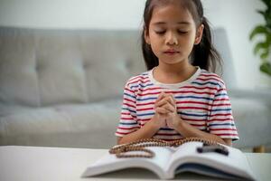 Christian concept. Little Asian girl praying withholding the cross. Concepts of hope, faith, Christianity, religion, photo