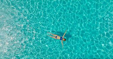 parte superior abajo ver de un mujer en azul traje de baño acostado en su espalda en el piscina. video