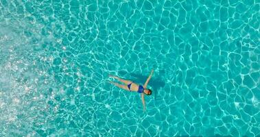 Top down view of a woman in blue swimsuit lying on her back in the pool. video