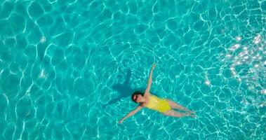 aéreo ver de un mujer en amarillo traje de baño nadando en el piscina. verano estilo de vida video