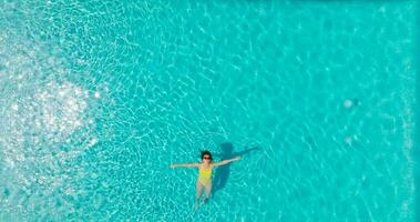 aéreo ver de un mujer en amarillo traje de baño nadando en el piscina. verano estilo de vida video