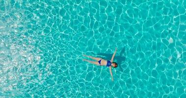 topo baixa Visão do uma mulher dentro azul roupa de banho deitado em dela costas dentro a piscina. video