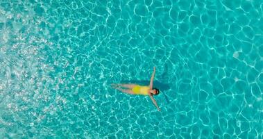 aéreo ver de un mujer en amarillo traje de baño nadando en el piscina. verano estilo de vida video