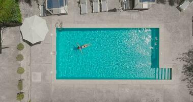 topo baixa Visão do uma mulher dentro azul roupa de banho deitado em dela costas dentro a piscina. video