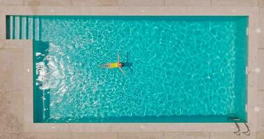 aéreo ver de un mujer en amarillo traje de baño nadando en el piscina. verano estilo de vida video