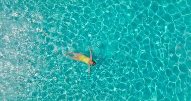 aéreo ver de un mujer en amarillo traje de baño nadando en el piscina. verano estilo de vida video