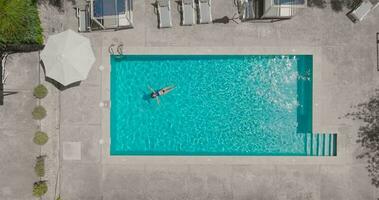 Top down view of a woman in blue swimsuit lying on her back in the pool. video