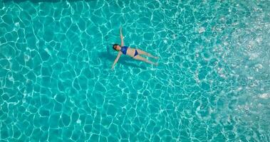 topo baixa Visão do uma mulher dentro azul roupa de banho deitado em dela costas dentro a piscina. video