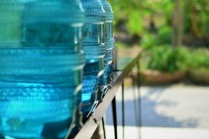 A row of large bottles of drinking water cooler put on the brown wood table. Selective focus, horizontal imager. photo