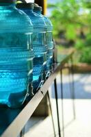 A row of large bottles of drinking water cooler put on the brown wood table. Selective focus, vertical image. photo