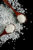 White rice in wooden spoons on black background. Raw grains of long rice. photo