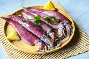 Fresco calamares pulpo o calamar para cocido comida a restaurante o Mariscos mercado, crudo calamar en plato con ensalada especias limón en de madera antecedentes foto