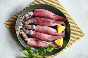 Raw squid on plate with salad spices lemon on wooden background, fresh squids octopus or cuttlefish for cooked food at restaurant or seafood market photo