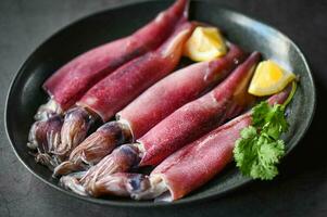 fresh squids octopus or cuttlefish for cooked food at restaurant or seafood market, Raw squid on plate with salad spices lemon on the dark plate background photo