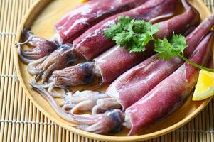 Raw squid on plate with salad spices lemon on wooden background, fresh squids octopus or cuttlefish for cooked food at restaurant or seafood market photo