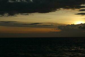A cloudy sky over the ocean with a dark sky and the sun setting behind it photo