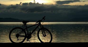 silueta de un bicicleta en contra el antecedentes de el puesta de sol en el lago foto