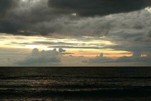 A cloudy sky over the ocean with a dark sky and the sun setting behind it photo