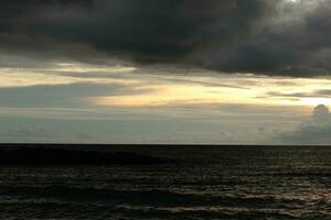 A cloudy sky over the ocean with a dark sky and the sun setting behind it photo
