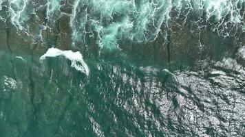 Aerial view of dark ocean waves with white wash. Brown reef with azure water covered by waves crashing into white sea foam. video