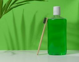 Refreshing mouthwash in a transparent plastic bottle and a wooden toothbrush on a green background photo