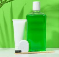 Refreshing mouthwash in a transparent plastic bottle and dental floss on a green background photo