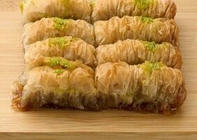 Pieces of baked baklava in honey and sprinkled with pistachios on a wooden board photo