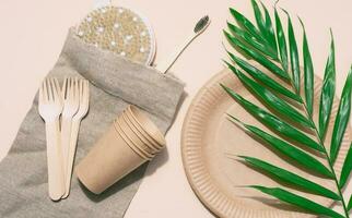 Paper plates, wooden forks and a toothbrush on a beige background, top view. Concept of recyclable garbage, zero waste photo