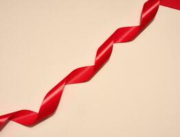 Red silk ribbon on a beige background, top view photo