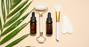 Brown glass bottle with a pipette, a white stone hand massager and a scraper for cosmetic procedures on a beige background, top view photo