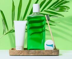 Refreshing mouthwash in a transparent plastic bottle and dental floss, white tube on a green background photo