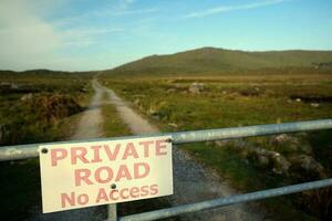 Closeup shot of sign private road, no access on the fence with country road and mountains in the background at Connemara National park in County Galway, Ireland photo