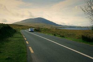 Beautiful landscape scenery with car driving on empty scenic road trough nature by the lough inagh with mountains in the background at Connemara National park in County Galway, Ireland photo