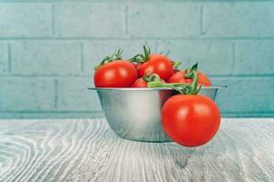 de cerca Disparo de sabroso rojo Tomates en acero cuenco en gris de madera mesa con ladrillo pared antecedentes foto