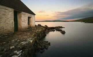 asombroso amanecer orilla del lago paisaje de del pescador choza reflejado en agua a pedregal en Connemara nacional parque ,condado Galway ,Irlanda foto