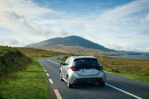 Beautiful landscape scenery with car driving on empty scenic road trough nature by the lough inagh with mountains in the background at Connemara National park in County Galway, Ireland photo