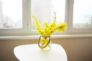 A bouquet of yellow flowers in a vase stand on a white table photo