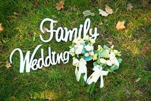 el palabra matrimonio y el familia desde un árbol en verde césped y nupcial ramo de flores foto