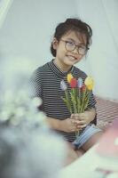 asiático niño participación artificial de tulipán flor en mano con dientes sonriente con felicidad foto