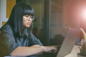 asian teenager sitting in working room and  reading message on computer laptop screen photo