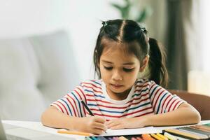 linda asiático niño niña dibujo con vistoso lapices a hogar foto