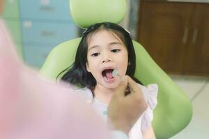 cerca arriba retrato de un caucásico niña teniendo un examen a el pediátrico dentista mientras sonriente a cámara foto