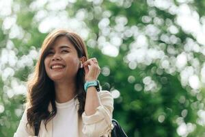 Portrait of a smiling young asian woman listening to music with earphones outdoors photo